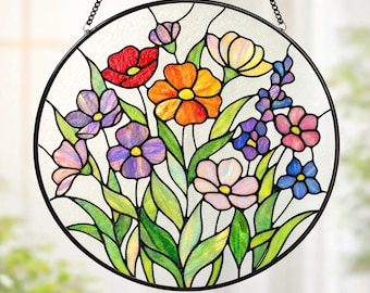 May include: A round stained glass window featuring a colorful floral design. The flowers include red, orange, yellow, purple, pink, and blue blooms with green leaves. The window is framed in black and hangs from a chain.