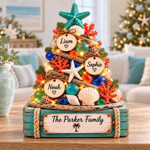 Peut inclure: Une décoration de sapin de Noël de table avec une étoile de mer turquoise au sommet, du corail, des coquillages et des sphères en verre. Trois ornements en bois portent les noms Liam, Sophie et Noah. La base est une boîte en bois turquoise marquée The Parker Family.