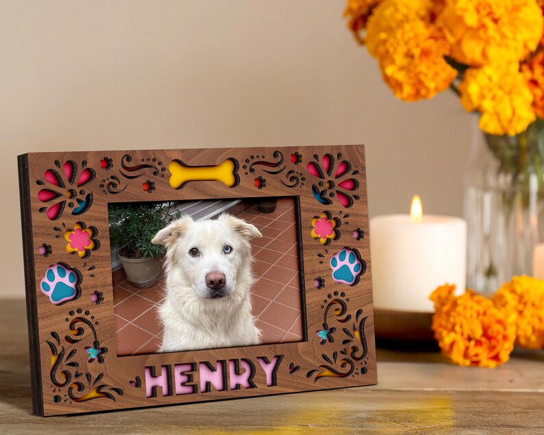 May include: A wooden photo frame with a picture of a white dog with blue eyes. The frame is decorated with colorful floral and paw print designs, and the dog's name, "HENRY," is displayed in pink letters.