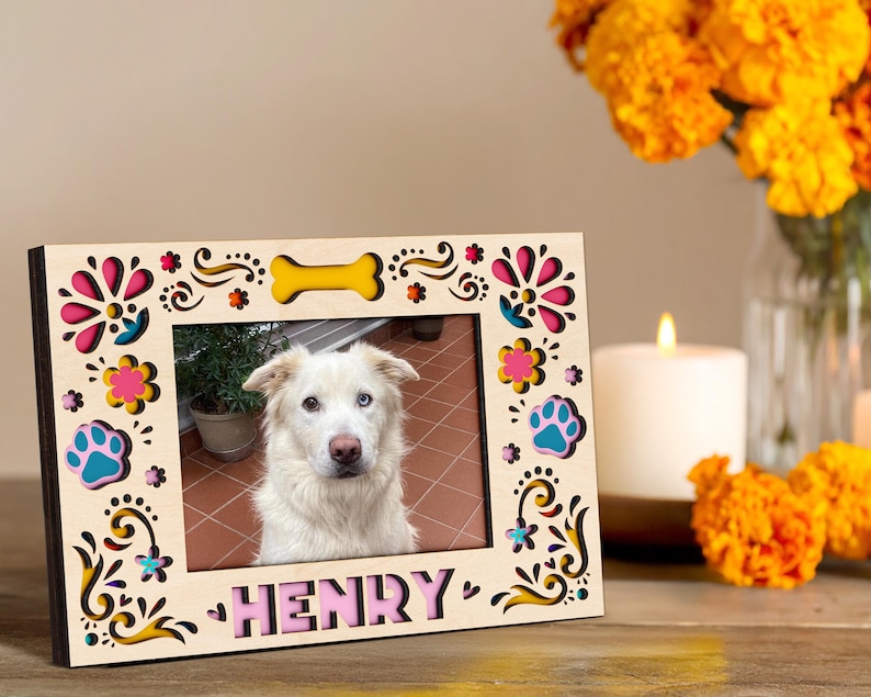 May include: A wooden picture frame with a photo of a dog named Henry. The frame is decorated with colorful floral and paw print cutouts. A yellow bone shape is at the top. The name "HENRY" is in pink letters at the bottom.