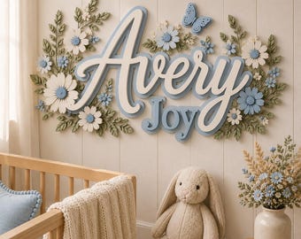 May include: A wall-mounted sign featuring the name Avery Joy in layered white and light blue script lettering. The sign is decorated with three-dimensional white and blue flowers, green leaves, and a small blue butterfly accent.