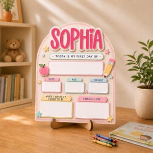 May include: An arched wooden sign with the name SOPHIA in pink letters at the top. It features sections labelled TODAY IS MY FIRST DAY OF, DATE, AGE, HEIGHT, WHEN I GROW UP I WANT TO BE, and THINGS I LOVE, decorated with a pink apple and a yellow pencil.