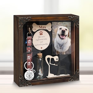 May include: A dark wooden pet memorial box containing a dog photo, collar, and a small bottle. The box features a bone-shaped plaque with the name "Max" and the years 2018-2025. The text "You were my favourite hello and my hardest goodbye" is also visible.