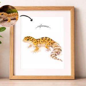Op de afbeelding: Waterverfprint van een luipaardgekko in een houten lijst. De gekko is geel en bruin met een patroon. Het woord "reference" staat boven de gekko. De print wordt gepresenteerd op een witte achtergrond.
