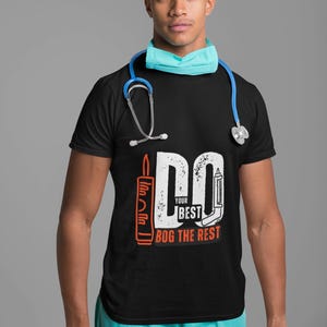 May include: Black t-shirt with the text "DO YOUR BEST BOG THE REST" in white and orange. The shirt features medical-themed graphics. The person in the image is wearing a surgical cap, mask, and has a stethoscope around their neck.