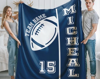 May include: A navy blue fleece blanket featuring a large white graphic of an American football, the text "TEAM NAME" arched above it, the number "15" below, and the name "MICHEAL" printed vertically in large white block letters.