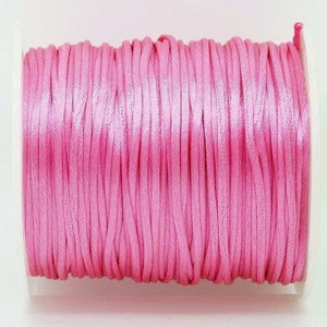 May include: A spool of pink waxed cotton cord. The cord is wound tightly around the spool and is ready to be used for crafting projects.