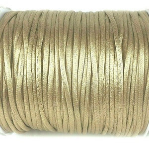 May include: A spool of beige satin cord, a type of thin, smooth, and lustrous cord often used for jewelry making and crafts.