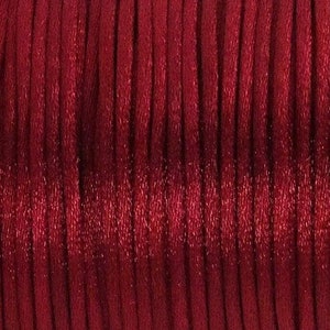 May include: A spool of red satin cord. The cord is wound tightly and has a slight sheen.