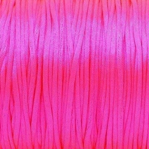 May include: A spool of pink and light pink waxed cord. The cord is wound tightly around the spool.