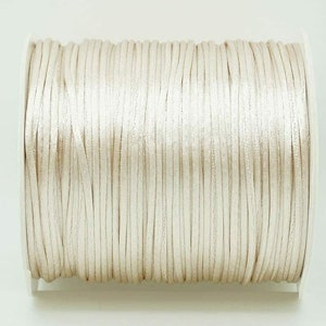 May include: A spool of off-white satin cord, a type of thin, flat, and smooth cord often used for crafts and jewelry making.