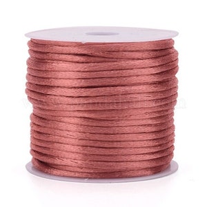 May include: A spool of dusty rose colored waxed cord. The cord is wound tightly around a white plastic spool.