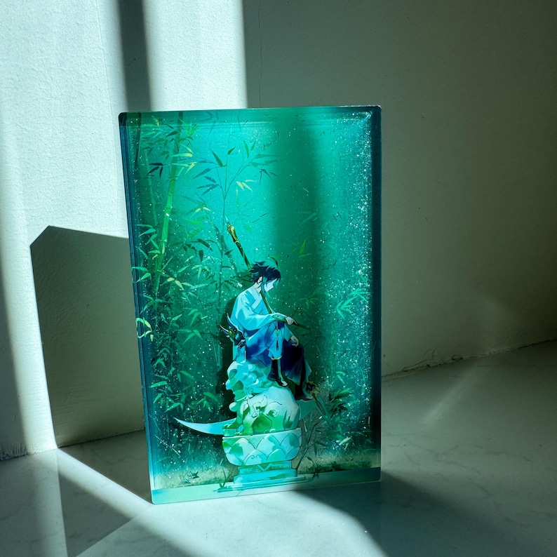 Peut inclure: Une &oelig;uvre d'art rectangulaire, de couleur sarcelle, repr&eacute;sentant une personne en robe bleue assise sur un socle d&eacute;coratif, entour&eacute;e de bambous. L'&oelig;uvre a une finition brillante et se d&eacute;tache sur un fond clair.
