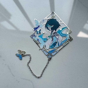 May include: A silver-toned bookmark featuring a diamond-shaped design with a character illustration and butterflies in shades of blue. A small butterfly charm is connected by a chain. The bookmark has intricate details and a decorative aesthetic.