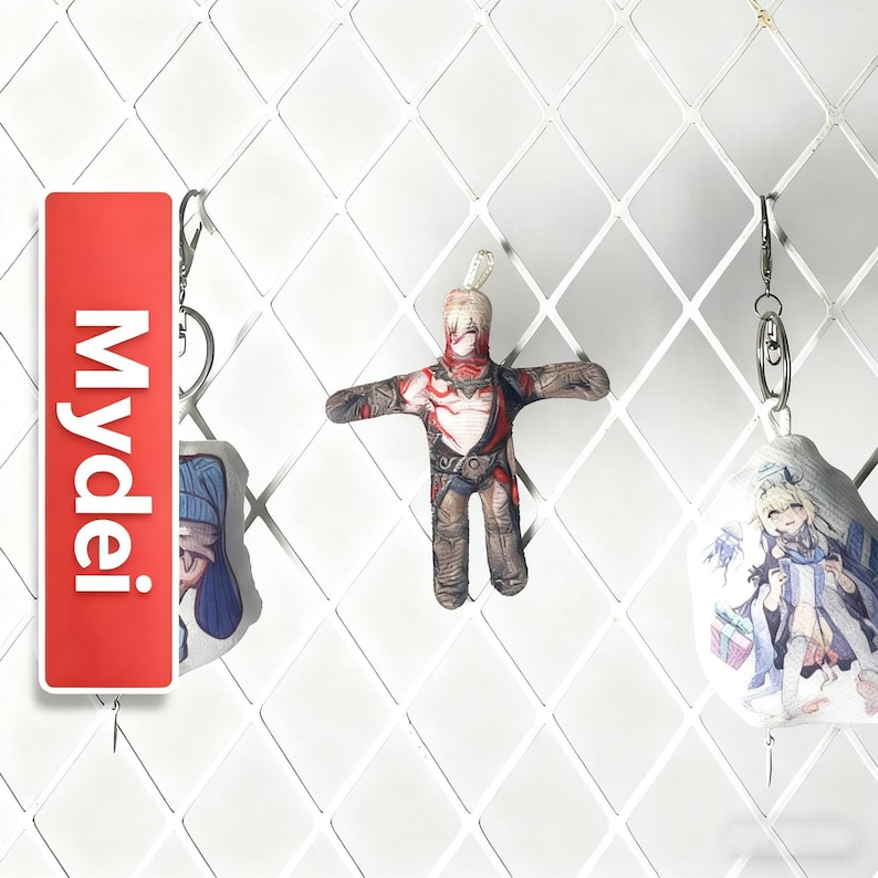 Op de afbeelding: Een verzameling sleutelhangers met anime-stijl personages en branding. E&eacute;n sleutelhanger is een rode rechthoek met het woord "Mydei" in het wit. Een andere is een kleine popachtige figuur met een rood en bruin ontwerp. De derde sleutelhanger heeft een karakterillustratie.