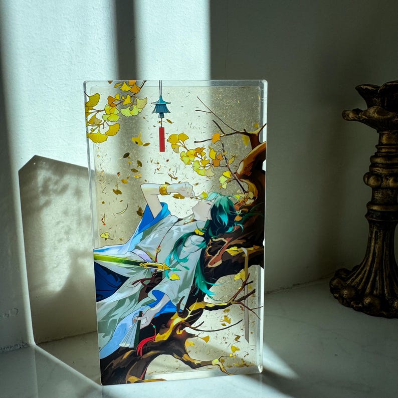 Peut inclure: Une pi&egrave;ce d'art rectangulaire en acrylique repr&eacute;sentant une illustration de style anime de deux personnages sous un arbre aux feuilles jaunes. Les personnages portent des v&ecirc;tements blancs et bleus. Une petite lanterne rouge est suspendue &agrave; l'arbre.