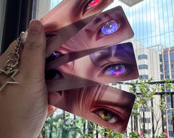 Könnte beinhalten: Ein Satz von vier rechteckigen Lesezeichen mit Nahaufnahmen von Augen im Anime-Stil in leuchtenden Farben. Die Augen haben rote, blaue, violette und grüne Iris. Ein silberner Schlüsselanhänger mit Sternanhänger ist befestigt.