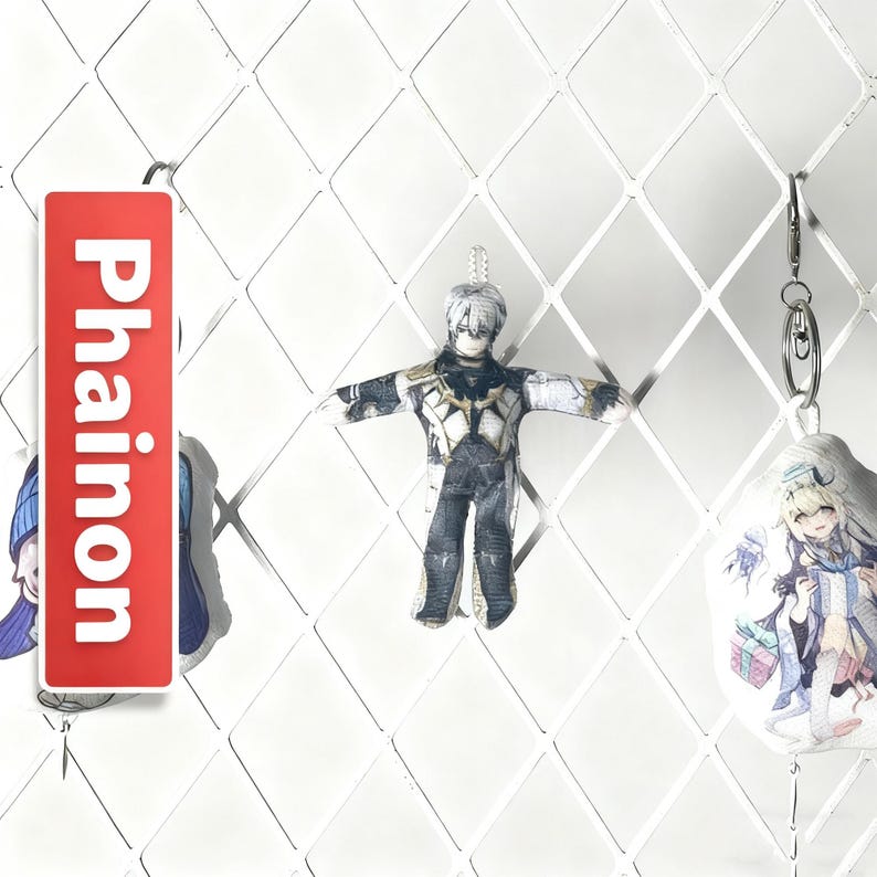 Op de afbeelding: Een verzameling sleutelhangers met anime-stijl personages. E&eacute;n sleutelhanger heeft het woord "Phainon" in het wit op een rode achtergrond. Een andere sleutelhanger is een kleine popachtige figuur met uitgestrekte armen. De derde sleutelhanger heeft een stripfiguur met een cadeau.