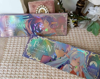 Könnte beinhalten: Zwei rechteckige Schachteln mit holografischen Designs. Auf einer Schachtel steht "RELIVE OLD DREAMS" und zeigt einen Anime-Charakter mit lila Haaren. Auf der anderen Schachtel steht "FRIEREN" und "PLEDGE" mit Anime-Charakteren. Die Schachteln befinden sich auf einer gemusterten Oberfläche.