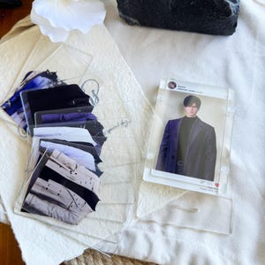 May include: Clear acrylic photo card holders with images of clothing and a person in a blazer. The holders are stacked and fanned out on a white surface. One holder has the name "Zayoe" and the text "Happy with me."