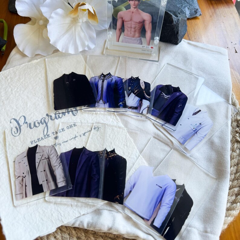 May include: A collection of clear plastic cards featuring images of various jackets and shirts in different colors and styles. The cards are arranged on a white cloth, with a card featuring a shirtless man. The text "Program" and "PLEASE TAKE ONE" is visible.