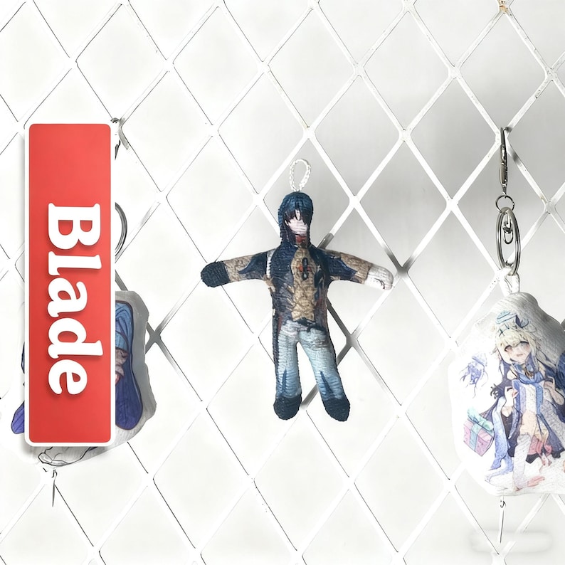 Op de afbeelding: Een rode rechthoekige sleutelhanger met het woord "Blade" in het wit, en twee karakter sleutelhangers. De centrale sleutelhanger is een kleine pop met een blauw en bruin outfit. De andere sleutelhangers tonen anime-achtige karakters.