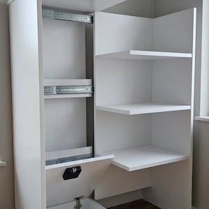 Puede incluir: Un armario de almacenamiento blanco y moderno con múltiples estantes y cajones. El armario tiene forma rectangular con una sección de estantes abiertos en el lado derecho. Los cajones tienen guías metálicas. Medidas en cm.