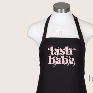 Puede incluir: Delantal negro con el texto "Always do you lash babe but let me do your lashes" en letras rosas.