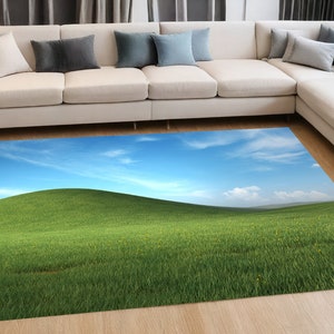May include: A green grassy field with a rolling hill in the background. The sky is blue with white clouds.