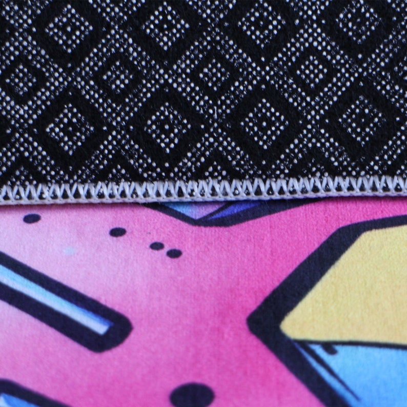 Peut inclure: Gros plan sur un tapis &agrave; motifs noirs et blancs avec un bord cousu blanc. Le tapis est pos&eacute; sur une surface &agrave; motifs roses, bleus et jaunes.