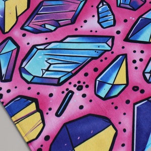 Peut inclure: Un tissu rose avec un motif r&eacute;p&eacute;titif de formes g&eacute;om&eacute;triques color&eacute;es ressemblant &agrave; des cristaux. Les cristaux sont dans des tons de bleu, violet, jaune et noir.