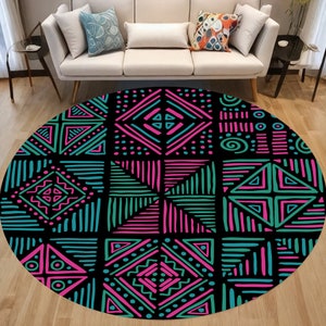 May include: A circular rug featuring a black backdrop with a geometric design in teal and pink. The pattern is composed of squares and diamond shapes, filled with lines, dots, and triangles. The rug is positioned on a wooden floor, in front of a white sofa.