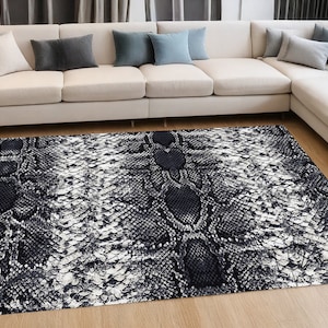 May include: A black and white snake skin patterned area rug. The rug has a subtle sheen and is laid out on a hardwood floor in front of a white sectional sofa.