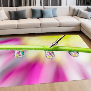 May include: Three pink and green flower petals are reflected in water droplets on a green stem. The droplets are suspended above a blurred background of pink and yellow.