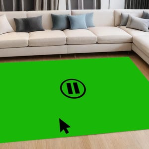 May include: A green area rug with a black pause button icon and a black arrow cursor. The rug is on a wooden floor in front of a white sectional sofa.