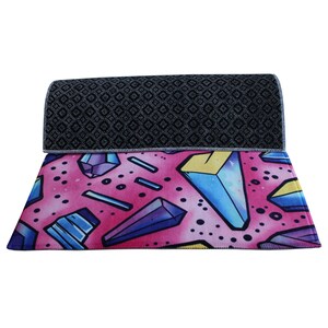 Peut inclure: Un tapis &agrave; motifs g&eacute;om&eacute;triques rose et bleu avec un dos &agrave; motifs diamants noirs et blancs. Le tapis a un bord arrondi.