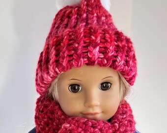 May include: A doll wearing a red knit hat with a white pom pom and a matching red knit scarf.