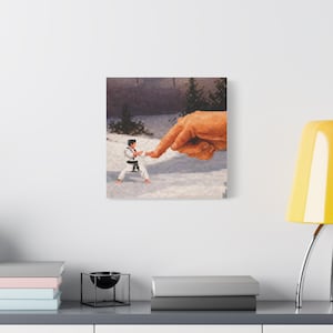 May include: A pixelated art print depicts a karate practitioner in a white uniform with a black belt, facing a giant pixelated hand. The background shows a snowy landscape with trees and a brick wall, creating a surreal, humorous scene.