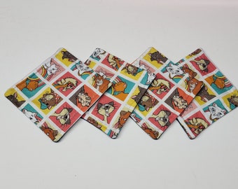 May include: Set of four square fabric coasters featuring a colorful pattern of cartoon cats from the Disney movie The Aristocats. The coasters are white with a multi-colored grid pattern and feature various cats in different poses.