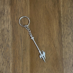 May include: A silver keychain featuring a trident with a winged design. The keychain is attached to a silver ring.