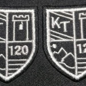 May include: Two white embroidered patches with a black background. Each patch features a shield with a tower, the letters "KT", and the number "120".