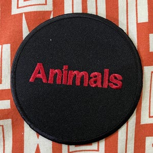 May include: A black circular patch with red embroidered text that reads "Animals".