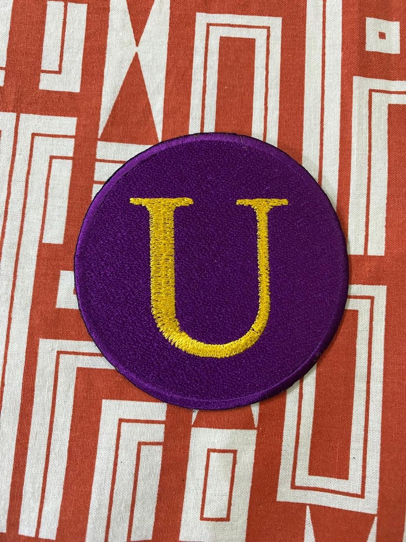 May include: A purple felt circle patch with a gold embroidered letter U.