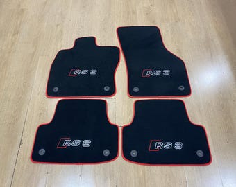 May include: Set of four black car floor mats with red trim. Each mat features the text "RS 3" in white and red. The mats are designed to fit a vehicle's footwells and have a textured surface.