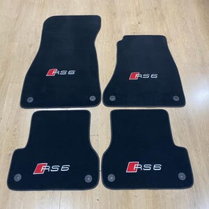 Puede incluir: Juego de cuatro alfombrillas negras para coche. Cada alfombrilla tiene el logotipo "RS6" en rojo y blanco. Las alfombrillas están diseñadas para proteger el interior del vehículo del polvo y el desgaste.