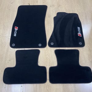 Puede incluir: Un juego de cuatro alfombrillas negras para coche. Las dos alfombrillas delanteras presentan el logotipo SQ5 bordado en blanco y rojo e incluyen ojales circulares de montaje. Las dos traseras son negras lisas con forma contorneada.