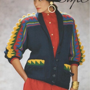May include: A navy blue cardigan with yellow, green, red, and blue geometric patterns on the sleeves. The cardigan has a collar, pockets, and buttons. The model is wearing a red shirt underneath.