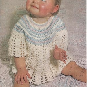 May include: A white crocheted baby dress with blue and pink stripes around the neckline. The dress has a lacy pattern and short sleeves.