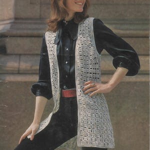 Può includere: Un lungo gilet all'uncinetto con un motivo a punto quadrato. Il gilet è di colore beige chiaro e ha un collo a V.