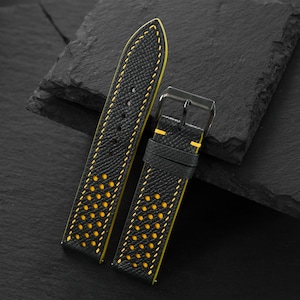 Puede incluir: Una correa de reloj de cuero negro con superficie texturizada, costuras en contraste de color amarillo brillante y una serie de perforaciones que revelan una capa inferior amarilla. Incluye una hebilla de metal negro y dos trabillas.